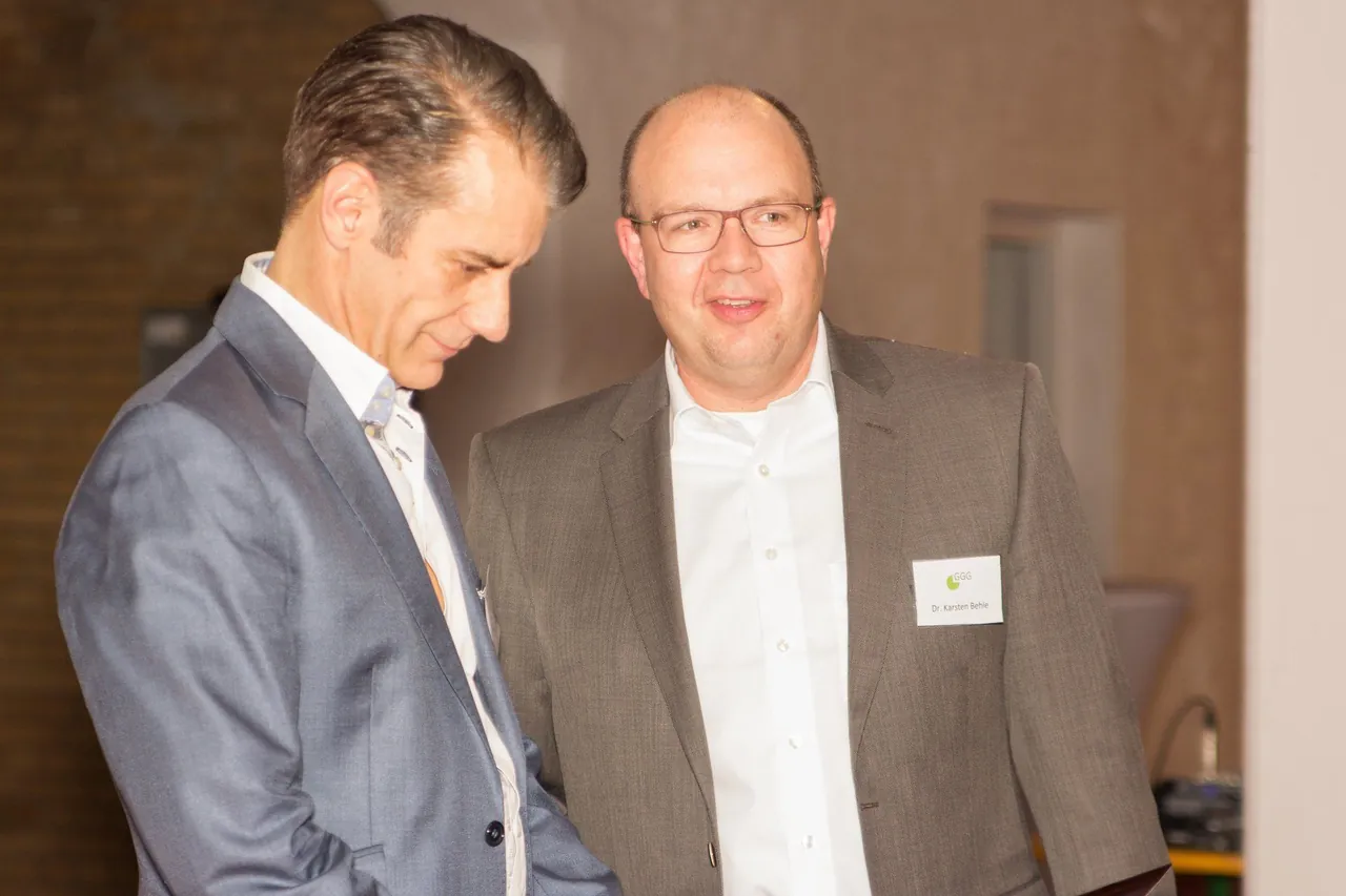 Zwei Männer im Gespräch, einer trägt ein GGG-Namensschild mit der Aufschrift „Dr. Karsten Behle“